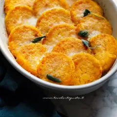 Gnocchi di zucca dorati e gratinati, guarniti con foglie di salvia, in una pirofila bianca.
