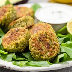 Polpette di spinaci dorate su un letto di spinaci freschi, con una ciotola di salsa e spicchi di lime.