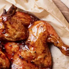 Pollo alla diavola succulento e dorato, con pelle croccante e lucida, servito su carta da forno.