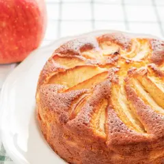 Torta di mele con yogurt, dorata e soffice, con mele a vista. Accanto, una mela rossa fresca.