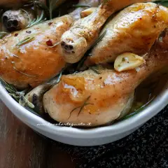 Succulenti fusi di pollo al forno, dorati e profumati con aglio e rosmarino, serviti in una ciotola bianca.