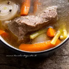 Un pezzo di carne succulenta cuoce lentamente in un brodo di carne aromatico, con carote, sedano e cipolla.