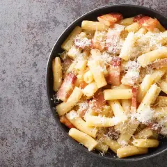 Rigatoni alla gricia fumanti, conditi con guanciale croccante e pecorino romano grattugiato, un classico della cucina romana.