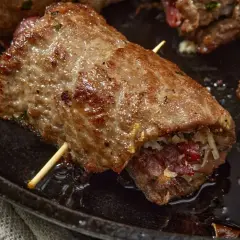 Involtini di carne in padella con sughetto, ripieni e cotti a puntino, pronti per essere gustati.