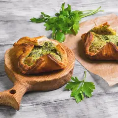 Due fagottini di pasta sfoglia con ripieno verde, uno su tagliere di legno, l'altro su carta forno. Idee su pasta sfoglia cosa mettere dentro.