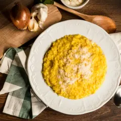 Un cremoso risotto alla milanese, spolverato di parmigiano, pronto per essere gustato. Accanto, cipolla e aglio, ingredienti essenziali.