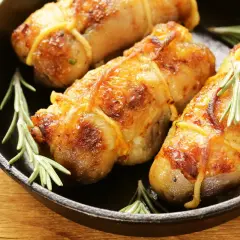 Involtini di pollo dorati e succulenti, legati con spago da cucina e guarniti con rametti di rosmarino, serviti in una padella di ghisa.