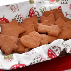 Cesto pieno di biscotti alla cannella a forma di stella, cuore e albero, su un telo natalizio.