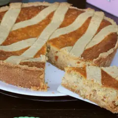 Una pastiera giallo zafferano, con una fetta servita su un piattino, pronta per essere gustata.