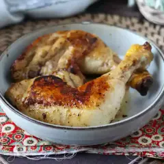 Cosce di pollo in padella, dorate e succulente, servite in una ciotola su un tovagliolo decorato.