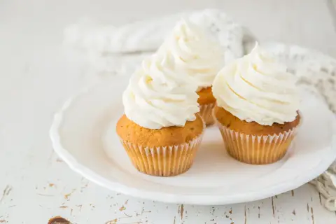 Tre cupcake su un piatto bianco, con abbondante crema al burro soffice e ariosa.