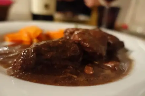 Un succulento brasato al barolo, tenero e profumato, accompagnato da carote arancioni su un piatto bianco.