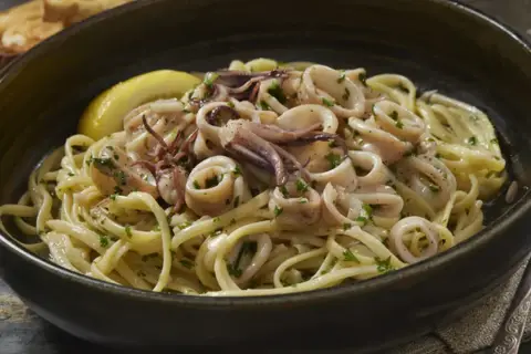 Un piatto invitante di pasta con calamari, guarnito con prezzemolo fresco e una fetta di limone.