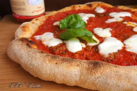 Pizza margherita con pomodoro, mozzarella filante e basilico fresco. La crosta dorata e alveolata è il risultato di una lunga lievitazione.