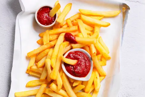 Patatine fritte dorate e croccanti con due ciotoline di ketchup fatto in casa, una con una patatina che si tuffa dentro.