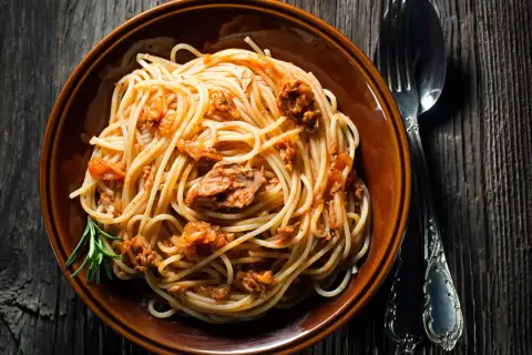 Un piatto di spaghetti al tonno, conditi con un sugo saporito e guarniti con un rametto di rosmarino, pronti per essere gustati.