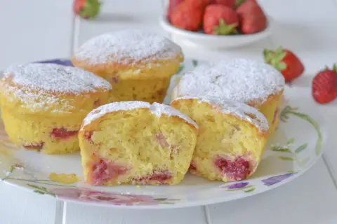 Morbidi muffin alle fragole, cosparsi di zucchero a velo, invitano a un dolce assaggio. Pezzi di fragola succosa si intravedono nell'impasto soffice.
