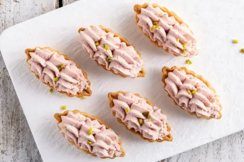 Piccoli cestini di pasta brisée ricetta, ripieni di crema rosa e guarniti con pistacchi.