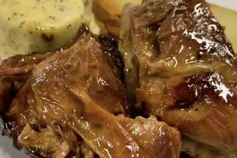 Succulento agnello al forno, dorato e lucido, servito con patate arrosto e una crema verde.