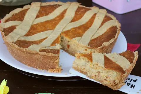 Una pastiera giallo zafferano, con una fetta servita su un piattino, pronta per essere gustata.
