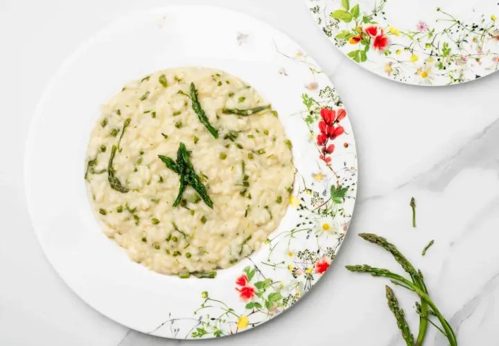 Un cremoso risotto con asparagi selvatici, guarnito con punte di asparago fresco su un piatto fiorito.