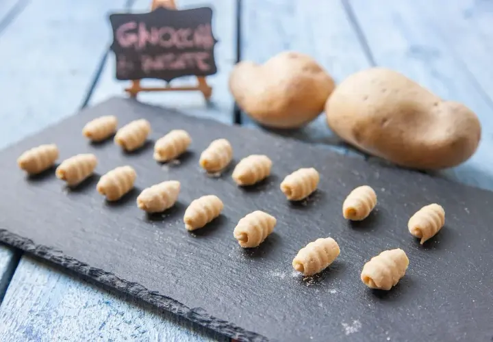 Gnocchi fatti in casa, morbidi e rigati, pronti per essere cucinati. Due patate sullo sfondo, ingredienti freschi per un piatto delizioso.