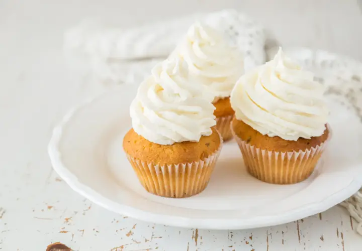 Tre cupcake su un piatto bianco, con abbondante crema al burro soffice e ariosa.