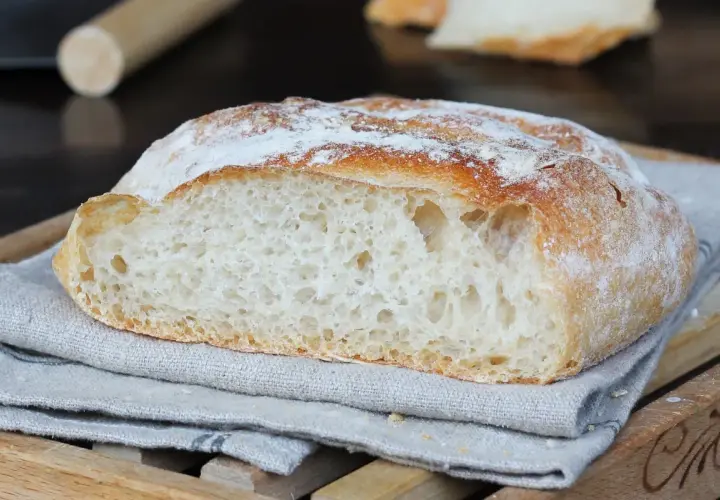 Pane fatto in casa, con crosta dorata e mollica alveolata, adagiato su un tovagliolo di lino.