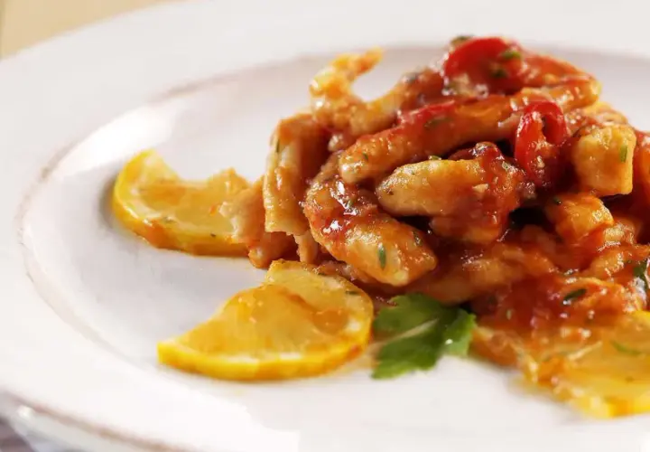 Straccetti di pollo al limone succulenti, conditi con salsa rossa e guarniti con fette di limone e prezzemolo fresco.
