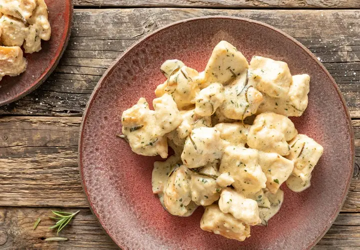Bocconcini di pollo al latte cremoso, conditi con erbe aromatiche, serviti su un piatto rustico.