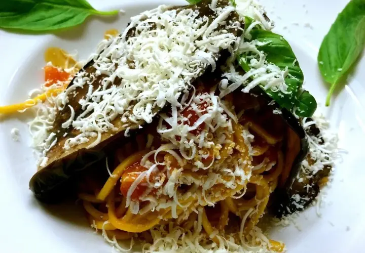 Pasta alla Norma ricetta: spaghetti con melanzane fritte, pomodoro e ricotta salata grattugiata, guarnita con basilico fresco.