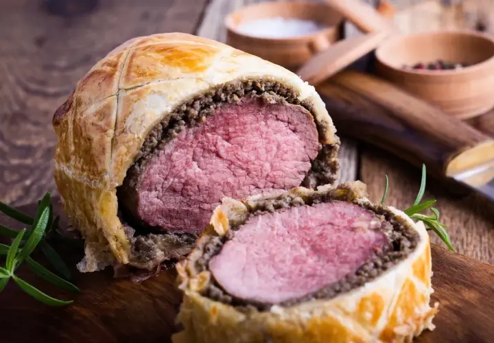 Un succulento filetto alla Wellington, tagliato a metà, rivela la sua carne rosa e tenera, avvolta in pasta sfoglia dorata e funghi.