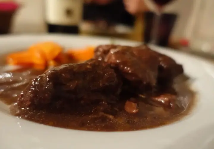 Un succulento brasato al barolo, tenero e profumato, accompagnato da carote arancioni su un piatto bianco.