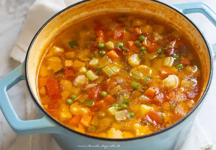 A close-up of a light blue pot filled with steaming minestrone soup, showing chunks of vegetables.