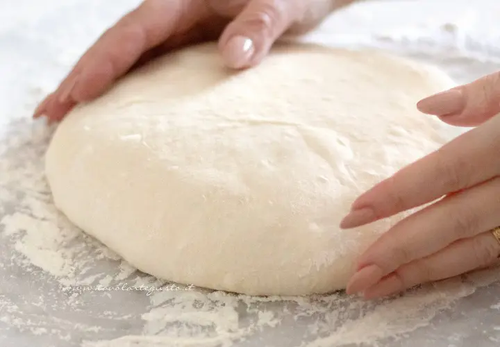Mani che lavorano un impasto soffice, pronto per diventare una pizza giallo zafferano.