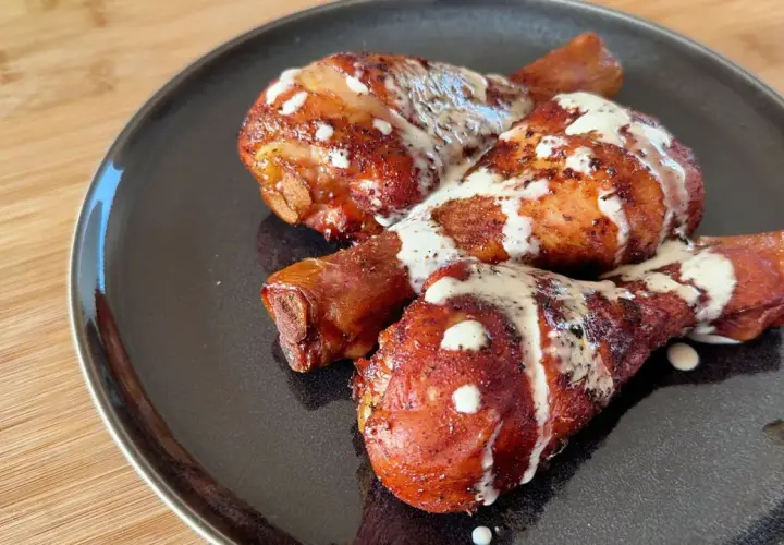Tre succulenti fusi di pollo arrostiti, conditi con spezie e nappati con una cremosa salsa bianca, serviti su un piatto scuro.