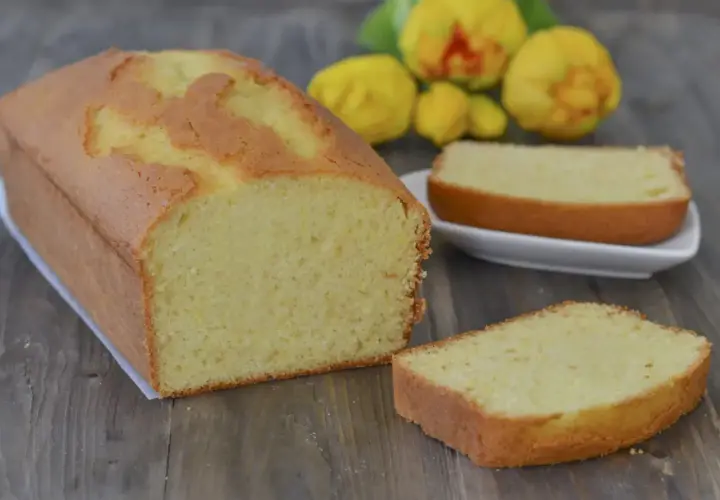 Plumcake al limone soffice e profumato, con una fetta tagliata e pronta da gustare. Sullo sfondo, limoni freschi.