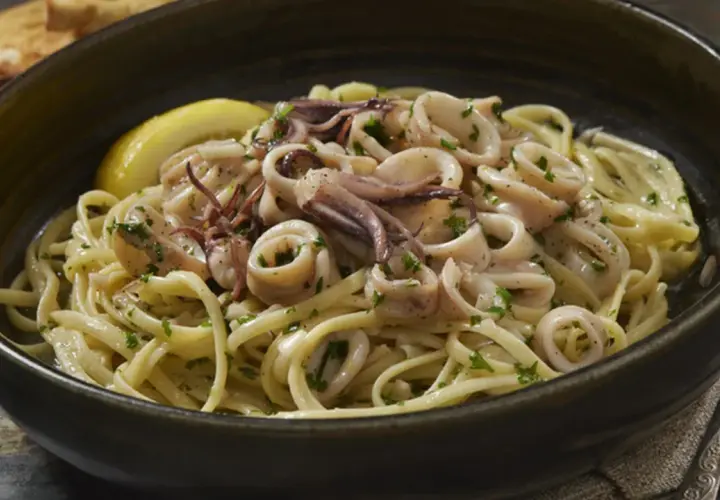 Un piatto invitante di pasta con calamari, guarnito con prezzemolo fresco e una fetta di limone.