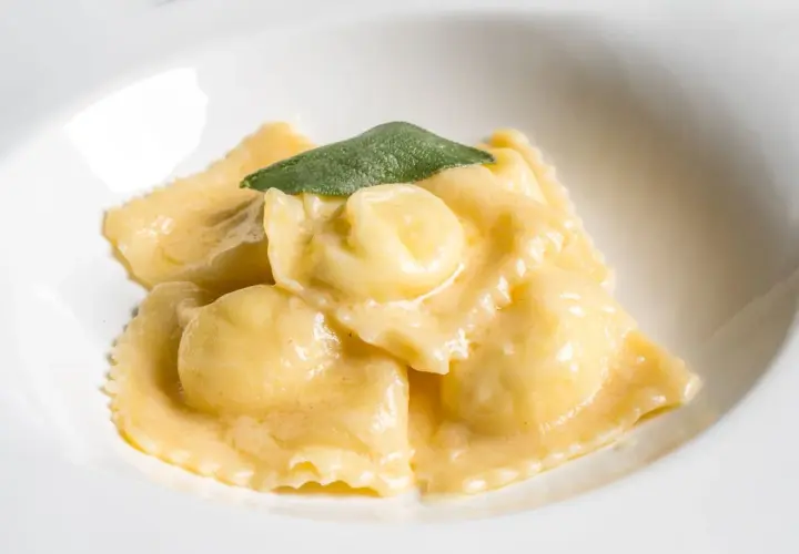 Ravioli dorati in salsa cremosa, guarniti con una foglia di salvia. Il ripieno per ravioli è un segreto gustoso.
