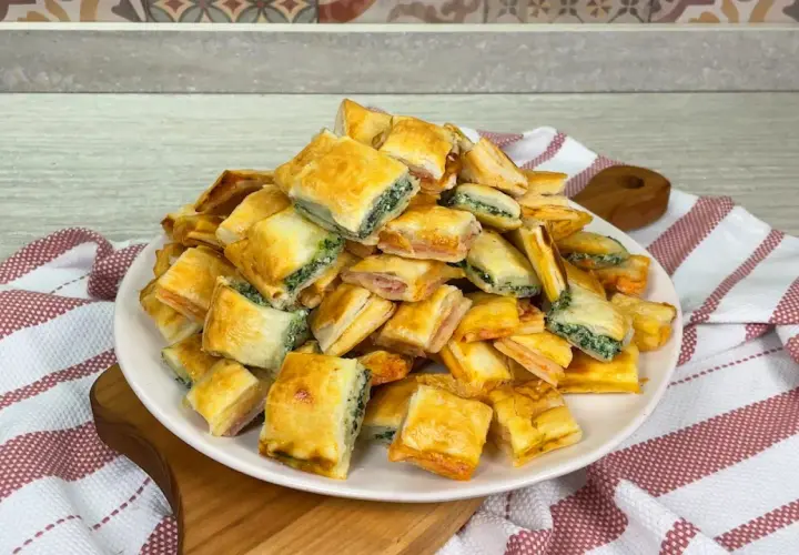 Un mucchio di salatini con pasta sfoglia, alcuni ripieni di spinaci e altri di prosciutto, pronti per essere gustati.