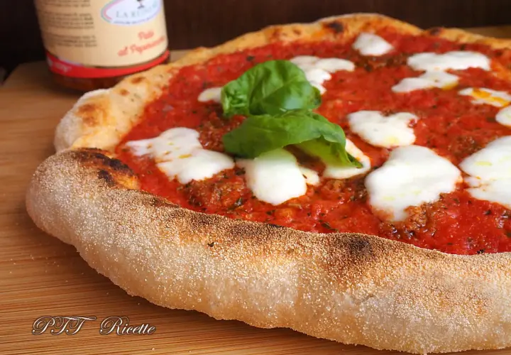 Pizza margherita con pomodoro, mozzarella filante e basilico fresco. La crosta dorata e alveolata è il risultato di una lunga lievitazione.