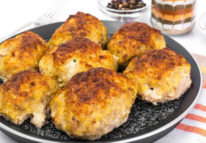 Golden brown zucchini and potato fritters on a black pan.