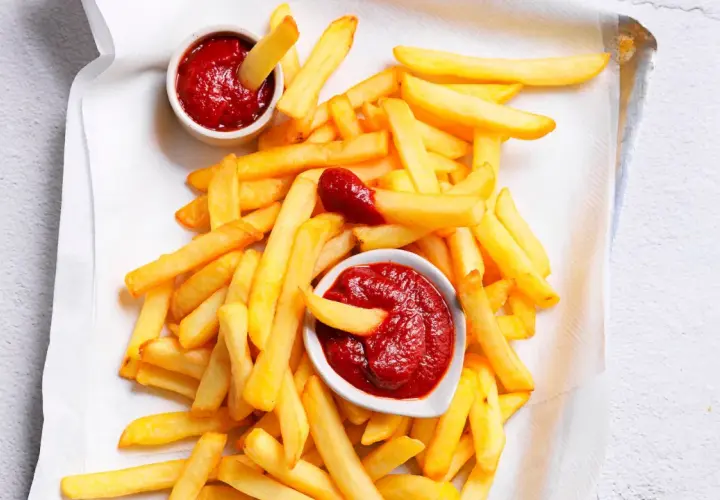 Patatine fritte dorate e croccanti con due ciotoline di ketchup fatto in casa, una con una patatina che si tuffa dentro.
