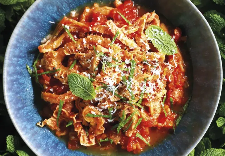 Un piatto fumante di trippa alla romana, condita con pomodoro, pecorino e menta fresca, servita in una ciotola blu.