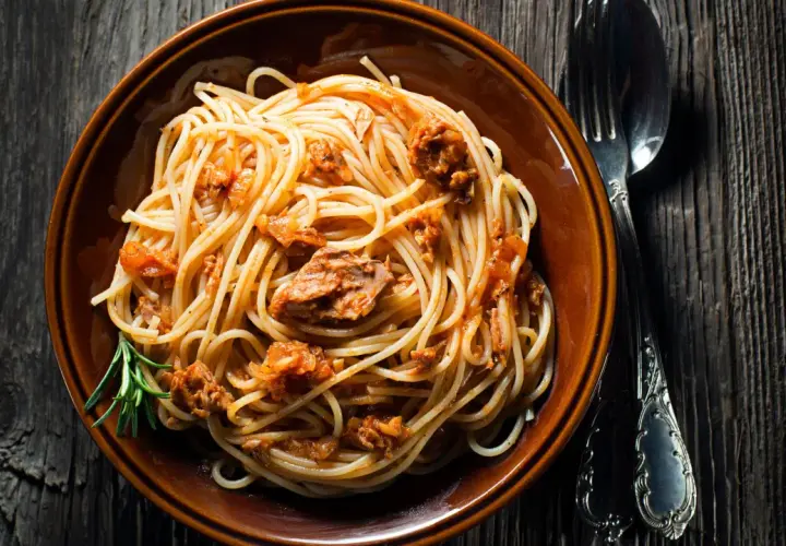 Un piatto di spaghetti al tonno, conditi con un sugo saporito e guarniti con un rametto di rosmarino, pronti per essere gustati.