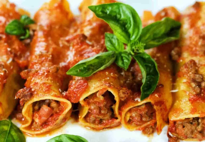 Cannelloni di carne ricetta della nonna, ripieni di ragù e conditi con sugo rosso e basilico fresco.