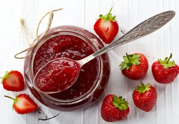 Un vasetto di marmellata di fragole fatto in casa, con fragole fresche e un cucchiaio pieno di dolcezza rossa.