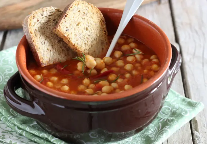 Una ciotola di terracotta con zuppa di ceci, pomodoro e rosmarino, accompagnata da fette di pane rustico.