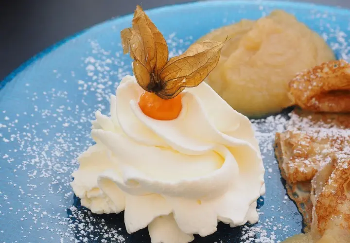 Panna montata soffice con physalis, su un piatto blu cosparso di zucchero a velo, accanto a un dolce che ricorda il pan di spagna.