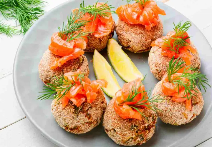 Polpette di pesce dorate, guarnite con salmone affumicato, aneto e spicchi di lime. Un antipasto raffinato e gustoso.